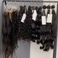 Hair extensions hanging on a rack with labels against a gray wall.