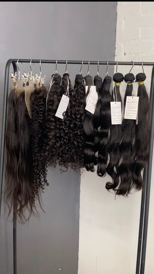 Hair extensions hanging on a rack with labels against a gray wall.