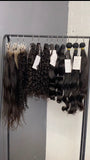 Hair extensions hanging on a rack with labels against a gray wall.